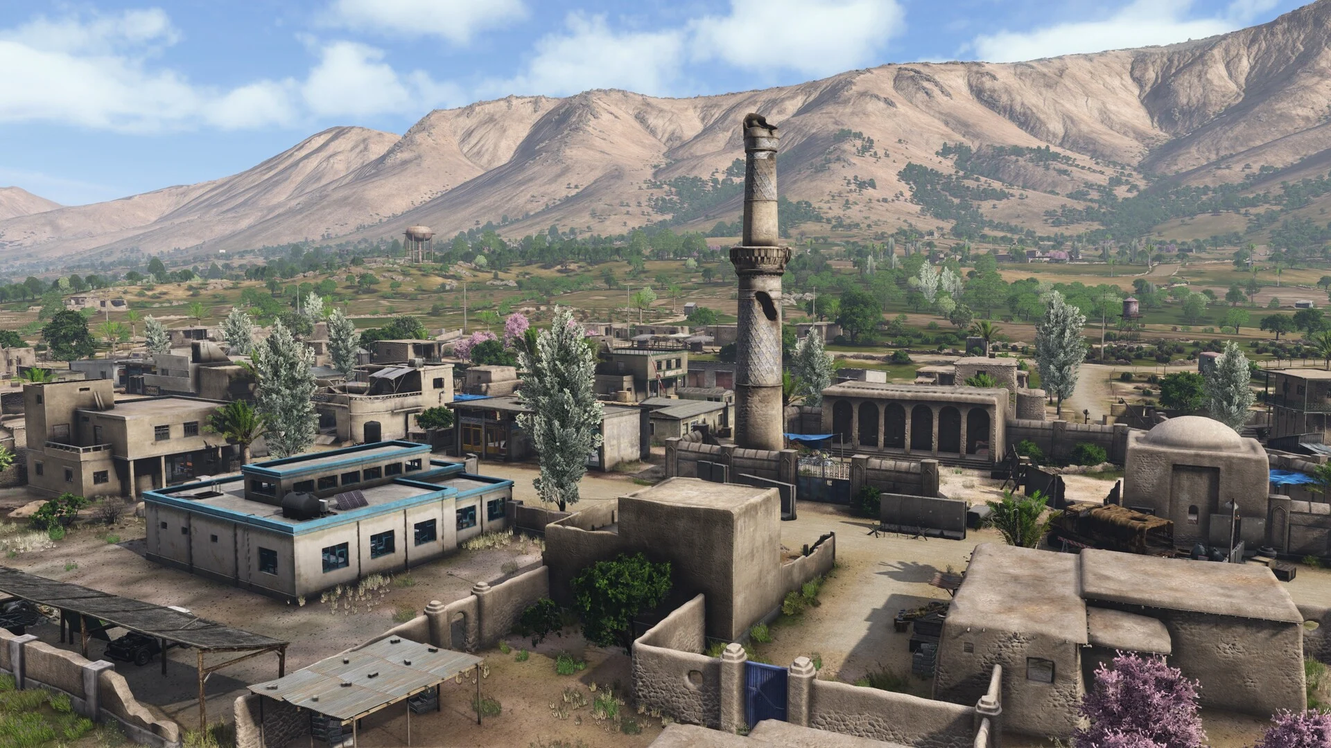 Nasdara rooftops, trees and a minaret beneath a mountain ridge.